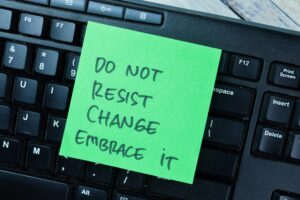 Green sticky note on a computer keyboard with message about embracing change