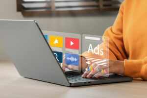 Person using a laptop with transparent digital advertising and media interface overlays, including ads, video, audio, and analytics icons.